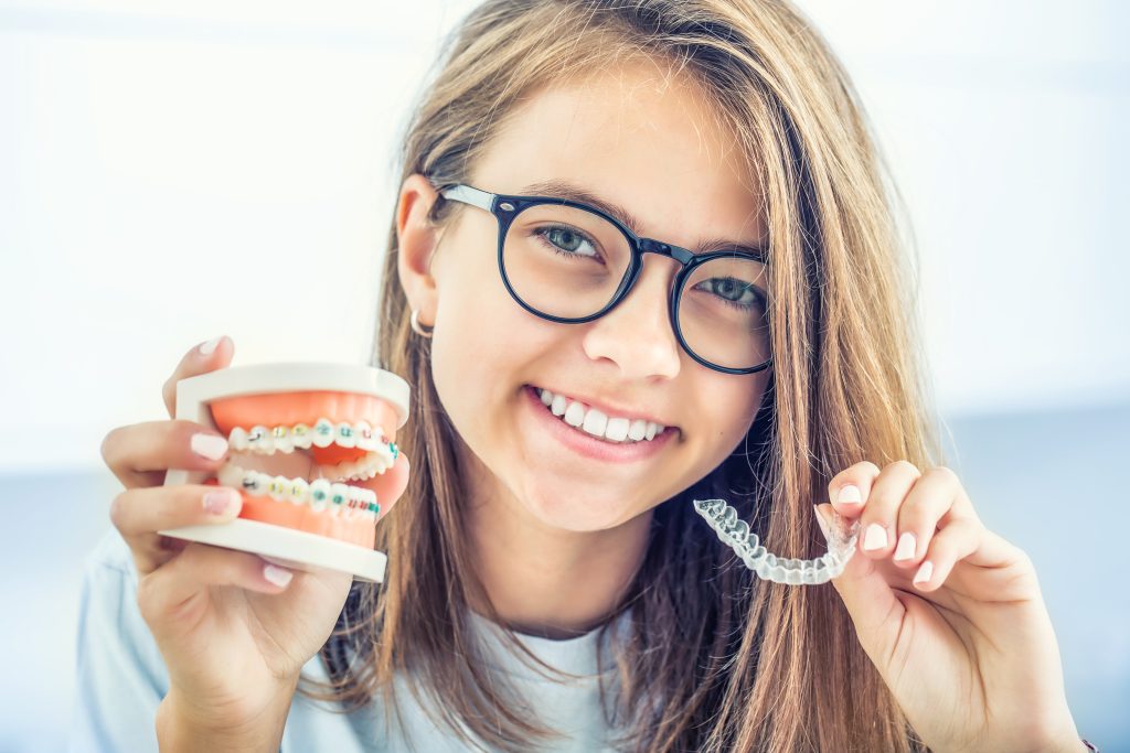 young girl holding dental braces model and clear invisalign tray