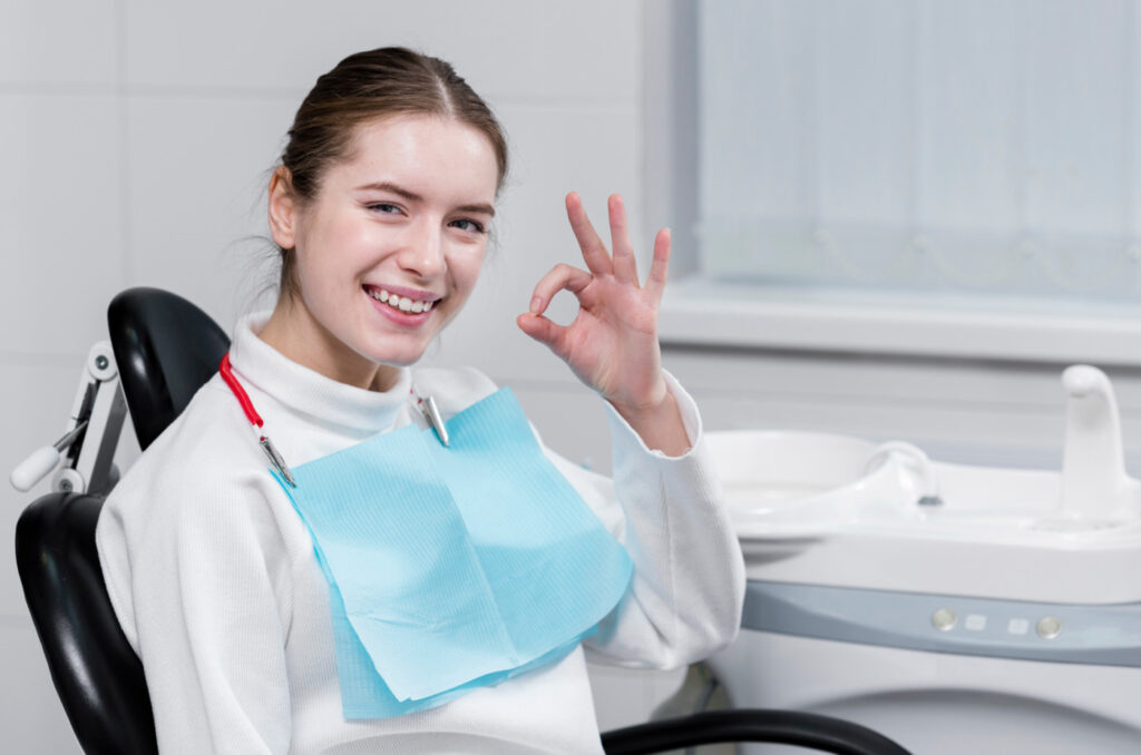 Smiling woman at dentist, giving okay sign.