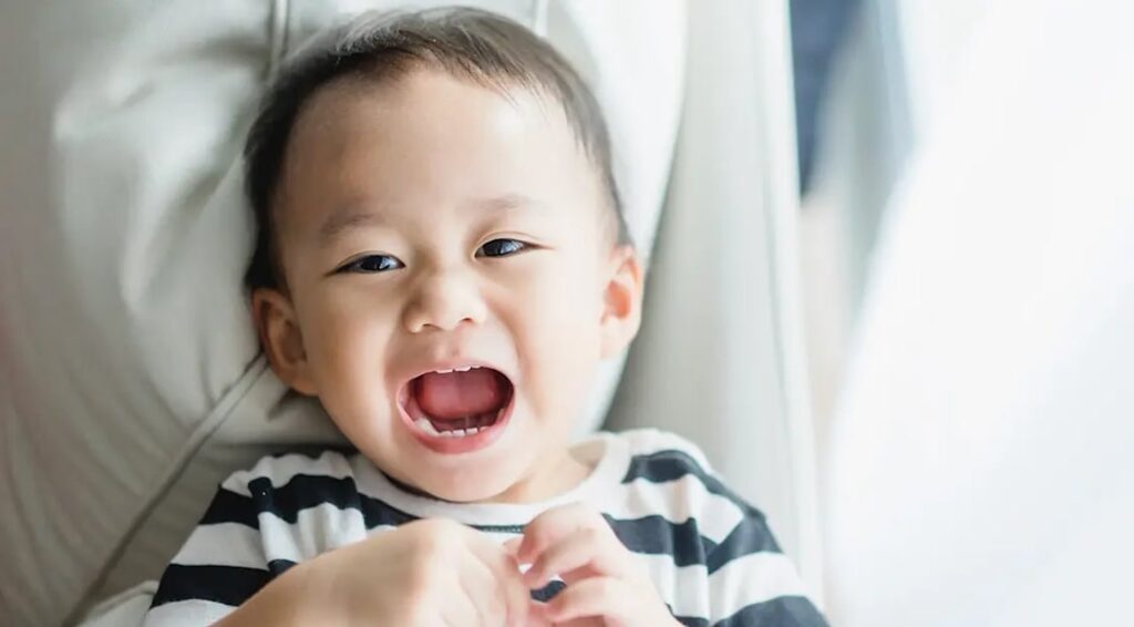 Smiling toddler with mouth open, showing teeth, wearing a black and white striped shirt